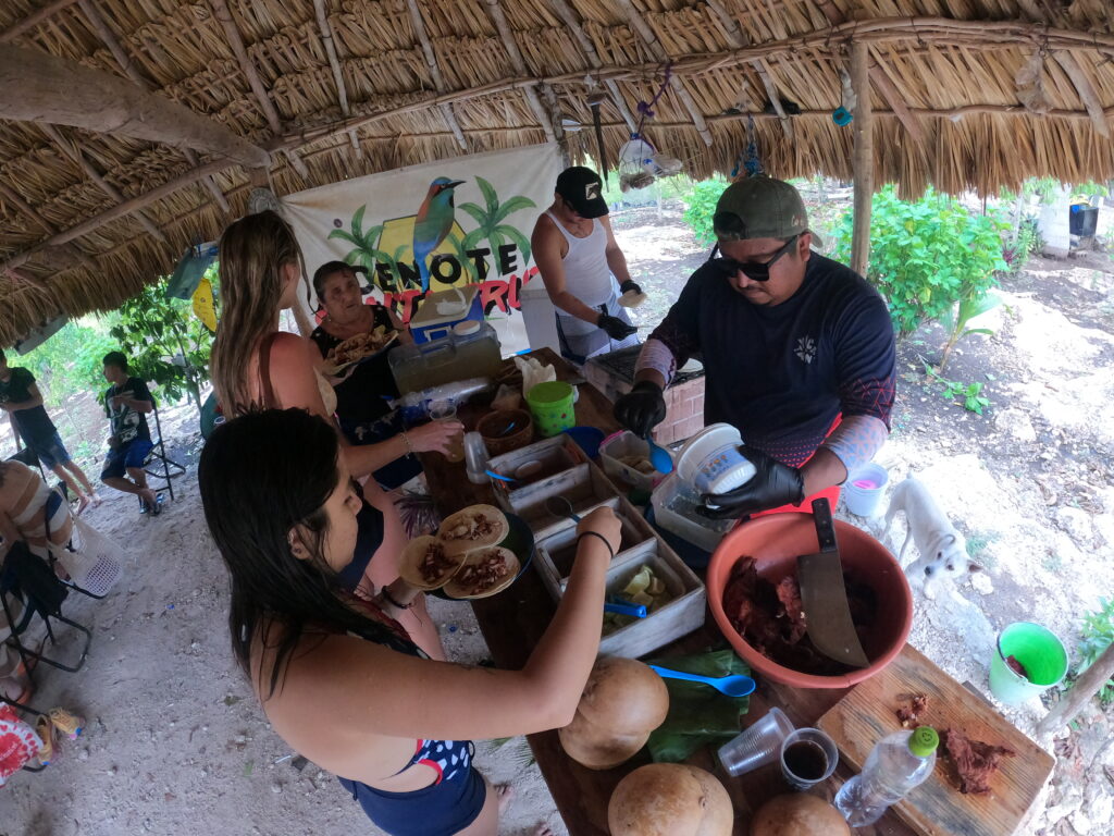 Viajeros compartiendo una comida tradicional bajo una palapa con anfitriones locales