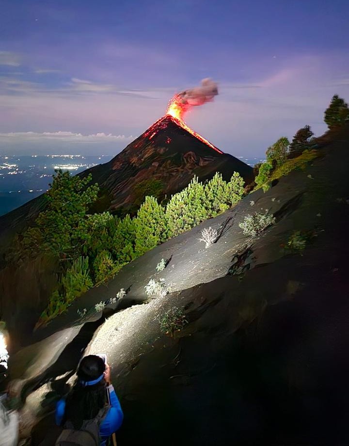 Viajera ascendiendo de noche el Acatenango con el Volcán de Fuego en erupción al fondo