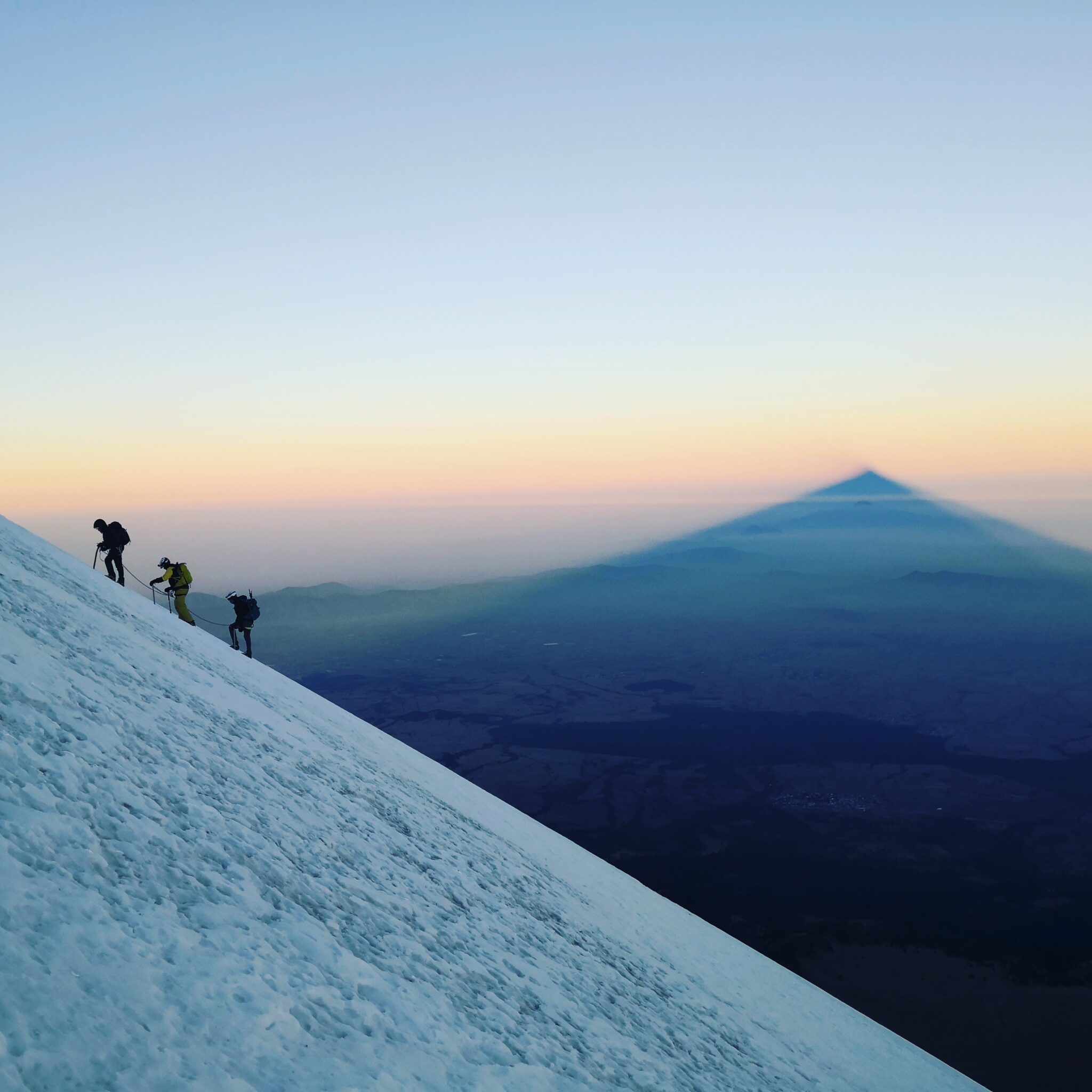 Montañistas ascendiendo el Pico de Orizaba al amanecer, con la sombra del volcán proyectada sobre las nubes