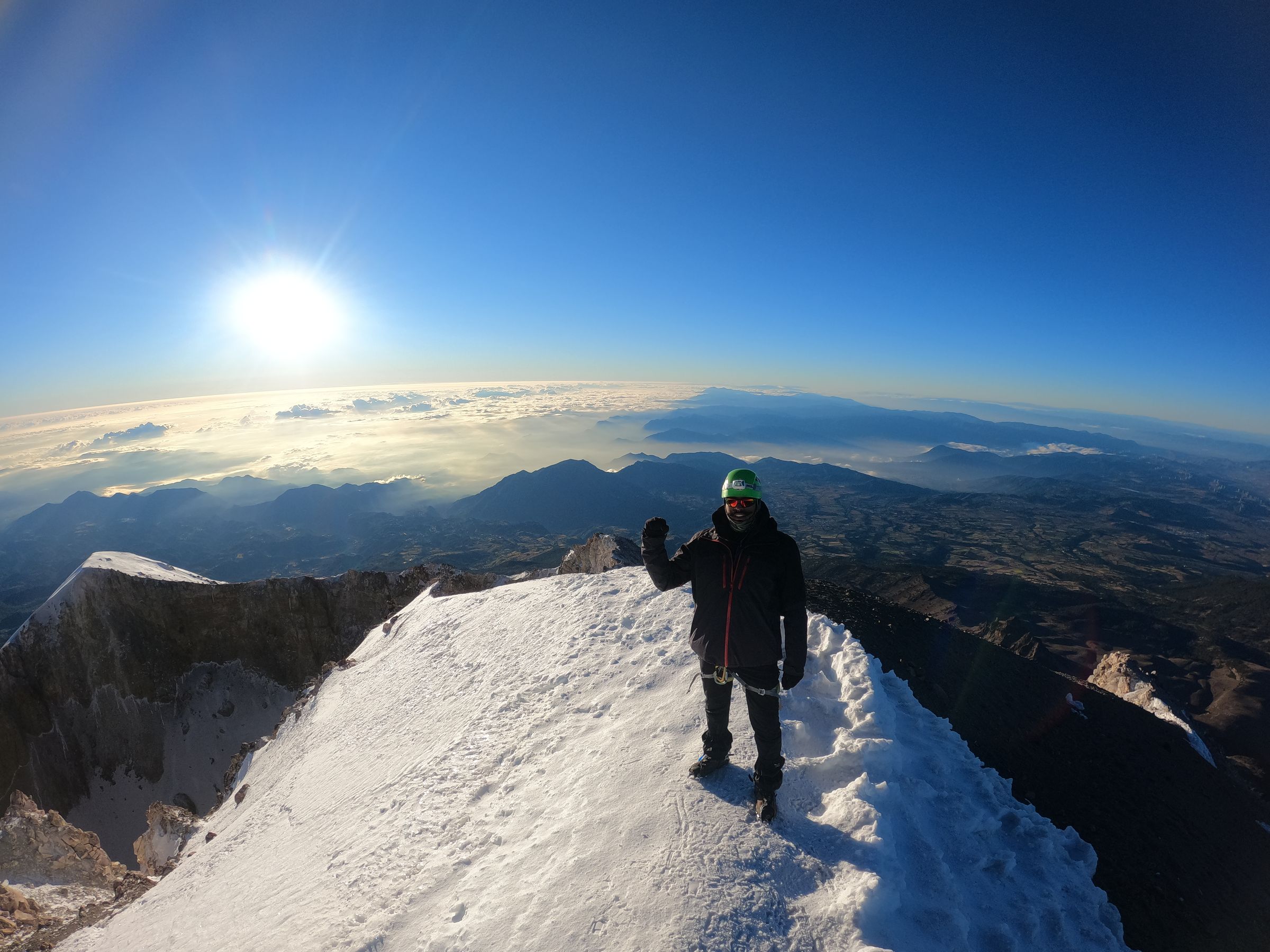 Odyssey guide on the summit of Pico de Orizaba at sunrise, above a sea of clouds