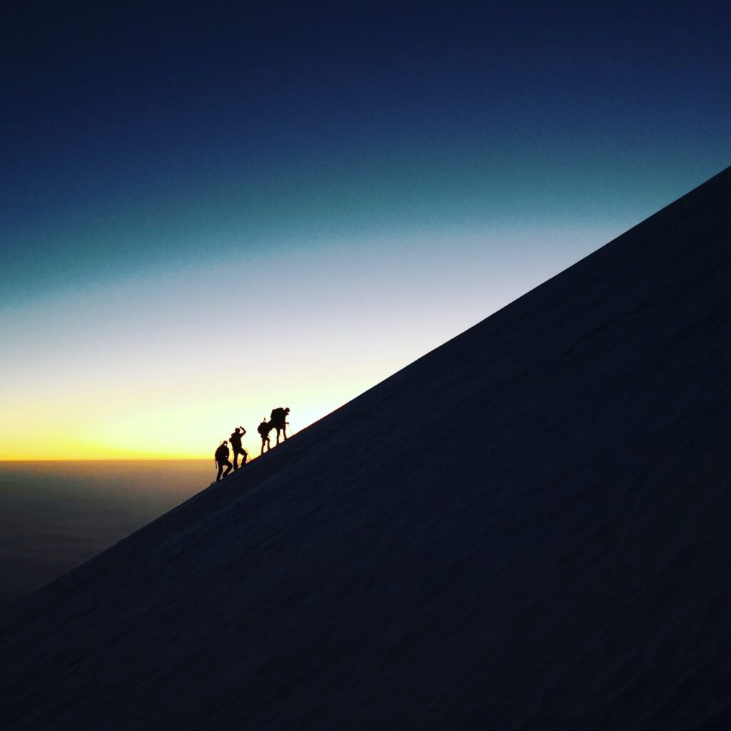 Silhouettes of four climbers ascending the snowy slope of Pico de Orizaba at sunrise