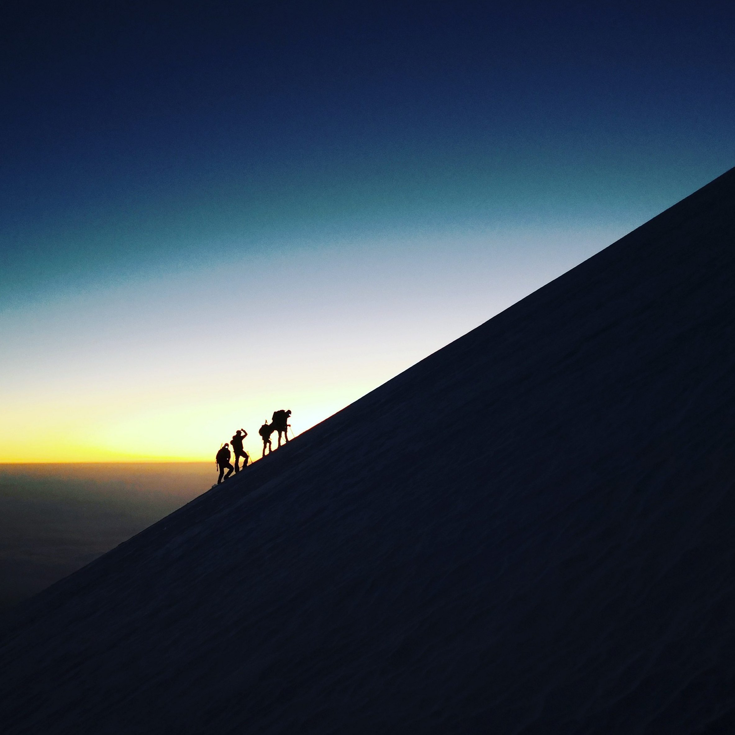 Silhouettes of four climbers ascending the snowy slope of Pico de Orizaba at sunrise